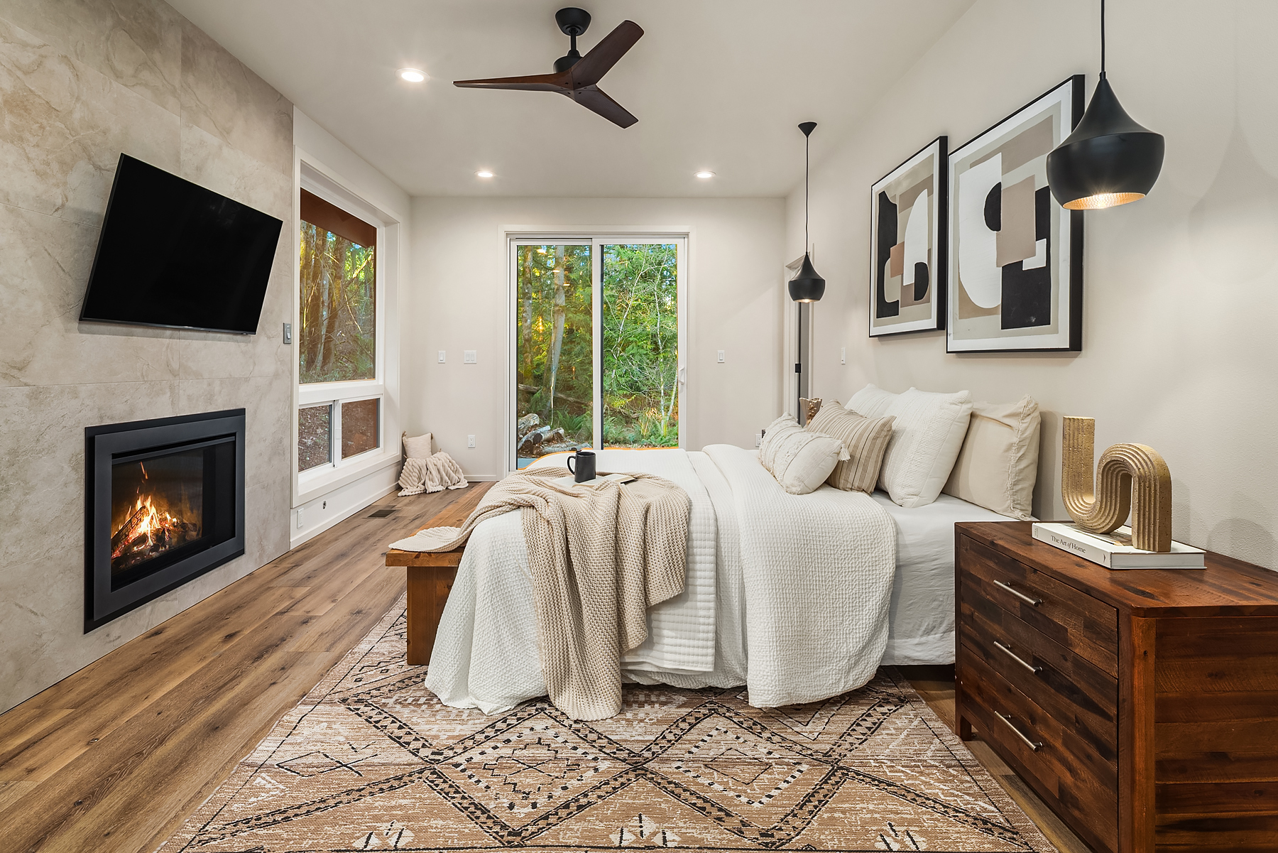 The primary bedroom with stone-clad fireplace, picture windows, and pendant lighting